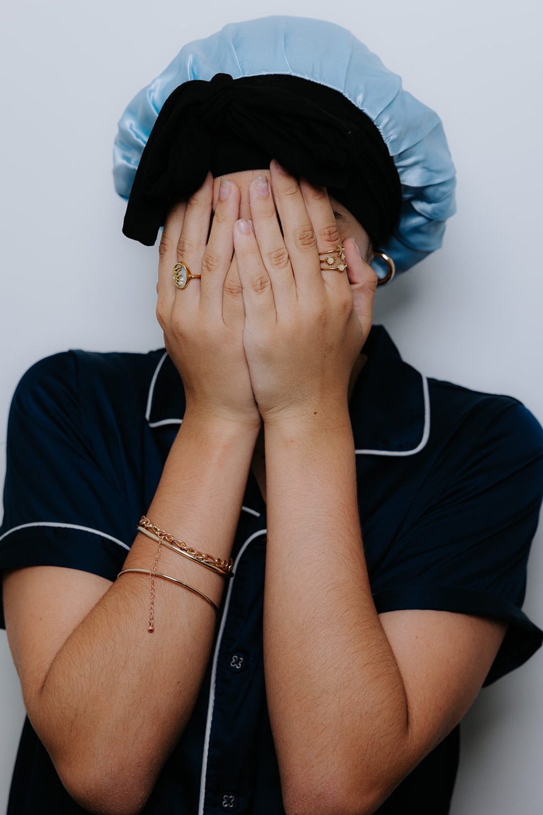 Person wearing a blue mulberry silk bonnet and navy pj's with jewelry on a plain background